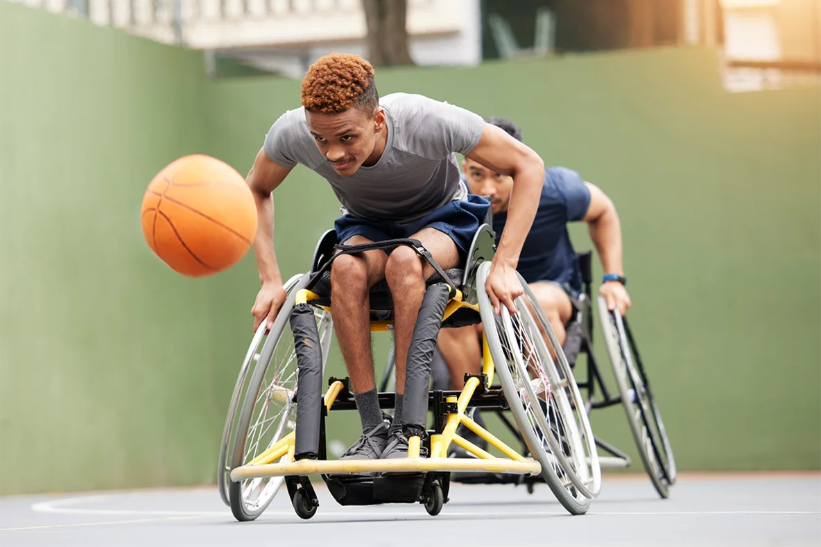 Zwei Rollstuhlbasketballer versuchen einen Basketball zu fangen
