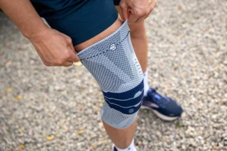 Abbildung einer Kniebandage: Person zieht sie sich gerade über das Knie