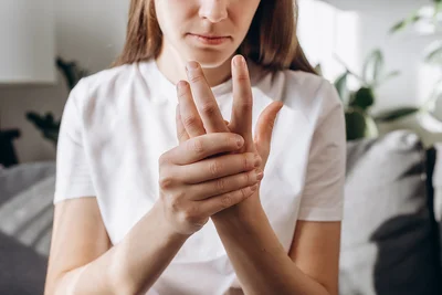 Abbildung einer Person, die sich ihre Hand hält. Das Gesicht ist dabei leicht schmerzverzerrt verzogen.