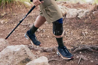 Person beim Wandern mit Wanderstöcken trägt eine Orthese