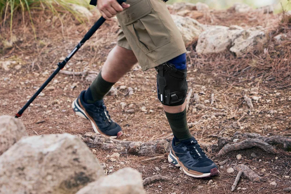 Person beim Wandern mit Wanderstöcken trägt eine Orthese
