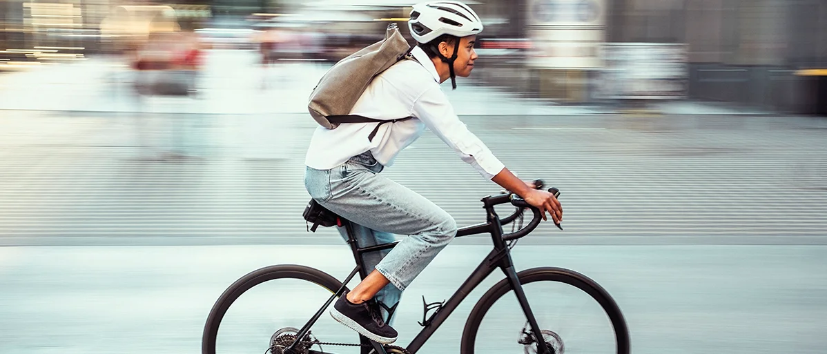 Junge Frau mit Helm auf dem Kopf fährt Fahrrad im Straßenverkehr in der Stadt.