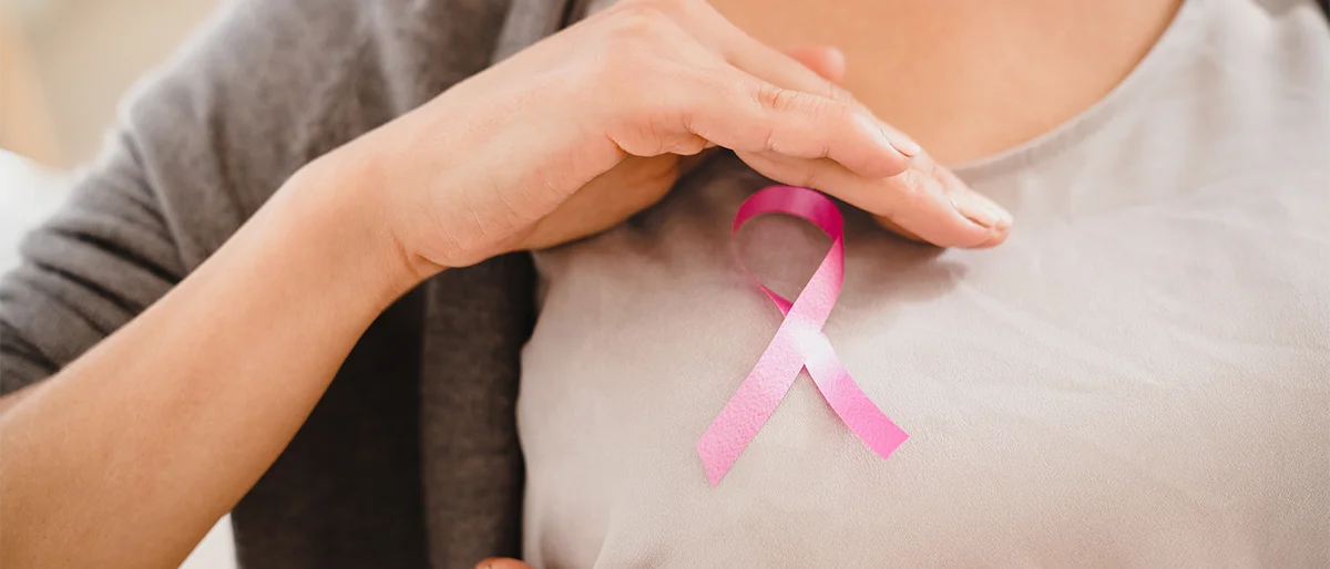Eine weibliche Person hat eine rosa Schleife auf der Brust. Die rosa Schleife steht symbolisch für Brustkrebs.