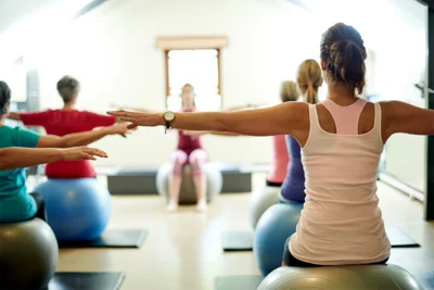 Person sitzt mit dem Rücken zum Betrachter auf einem Gymnastikball und streckt die Arme aus