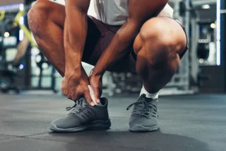 Person greift sich im Fitnessstudio mit beiden Händen an den Fuß-Knöchel