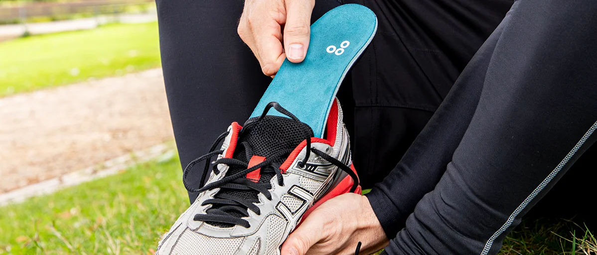Eine sportlich gekleidete Person legt eine orthopädische Einlage in einen Laufschuh