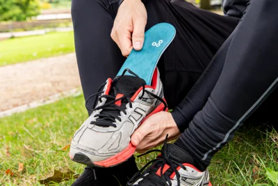 Eine sportlich gekleidete Person legt eine orthopädische Einlage in einen Laufschuh