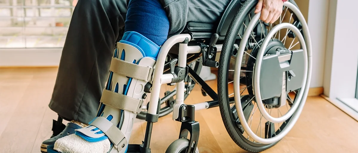 Person sitzt mit einem geschienten Bein im Rollstuhl
