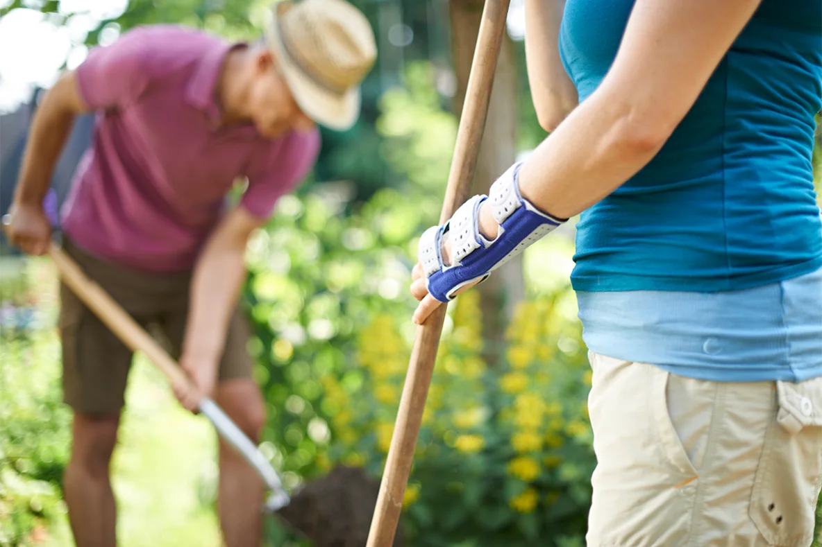 Frau arbeitet im Garten und trägt eine Orthese am Handgelenk