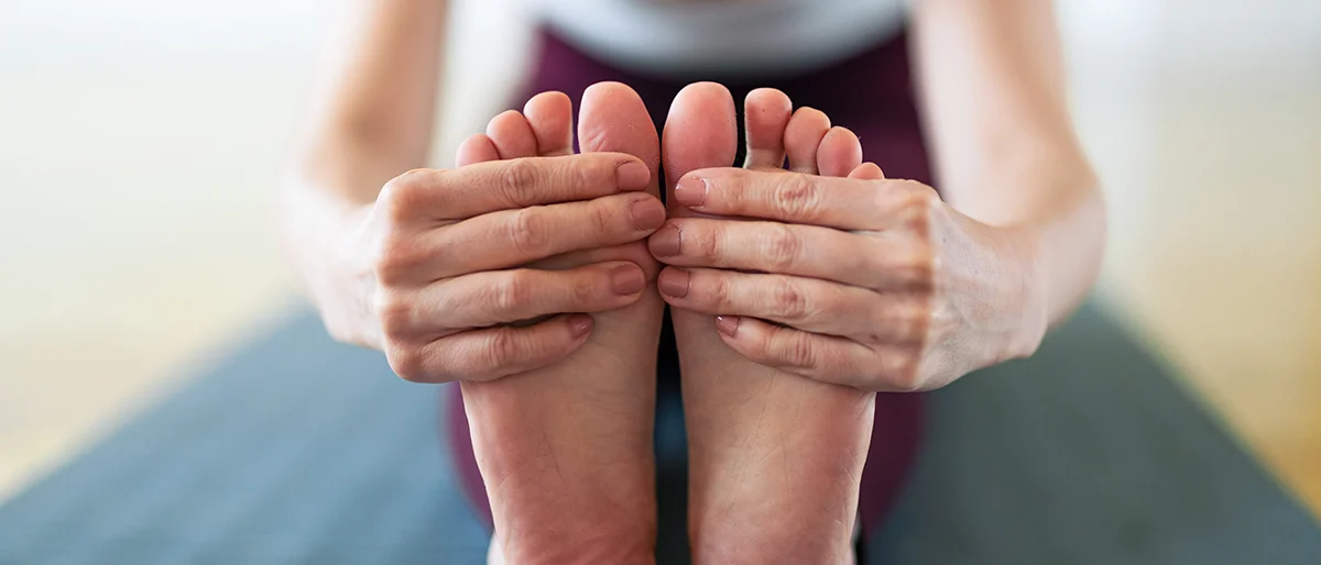 Person greift sich mit beiden Händen an die Füße