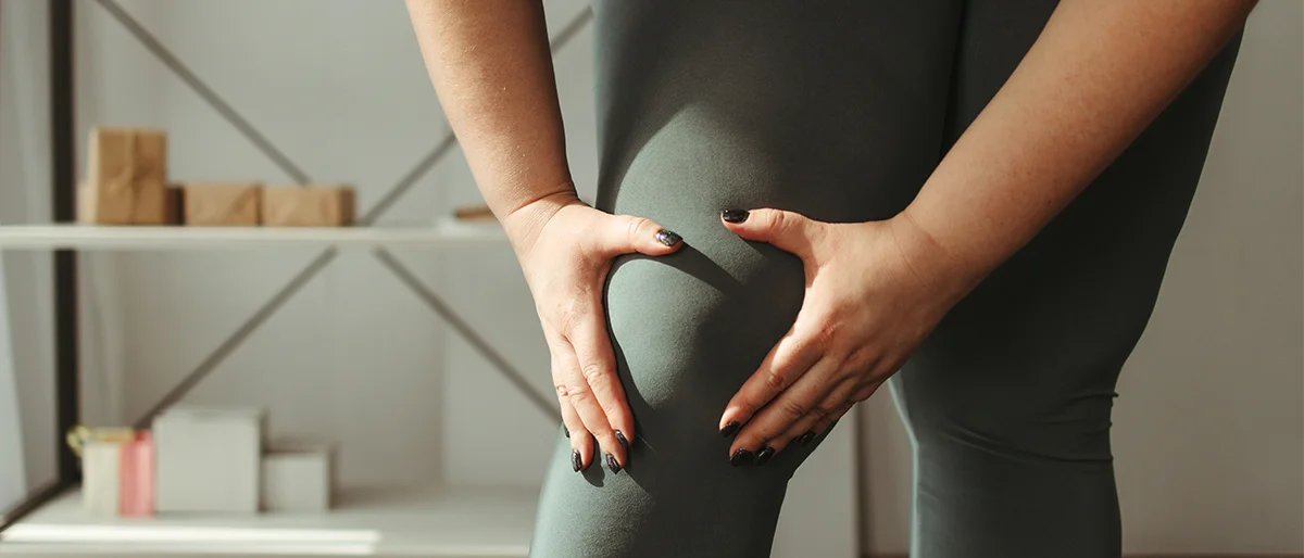 Sportlich gekleidete Person greift sich mit beiden Händen an ein Knie