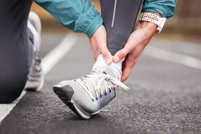 Person in Sportschuhen greift sich ans Sprunggelenk.