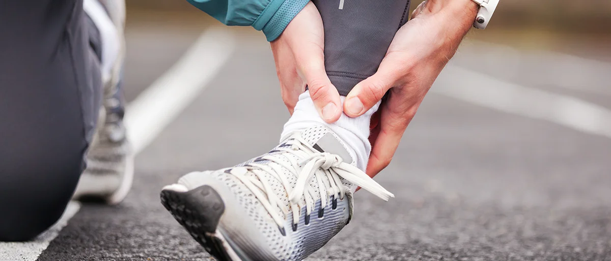 Person in Sportschuhen greift sich ans Sprunggelenk.