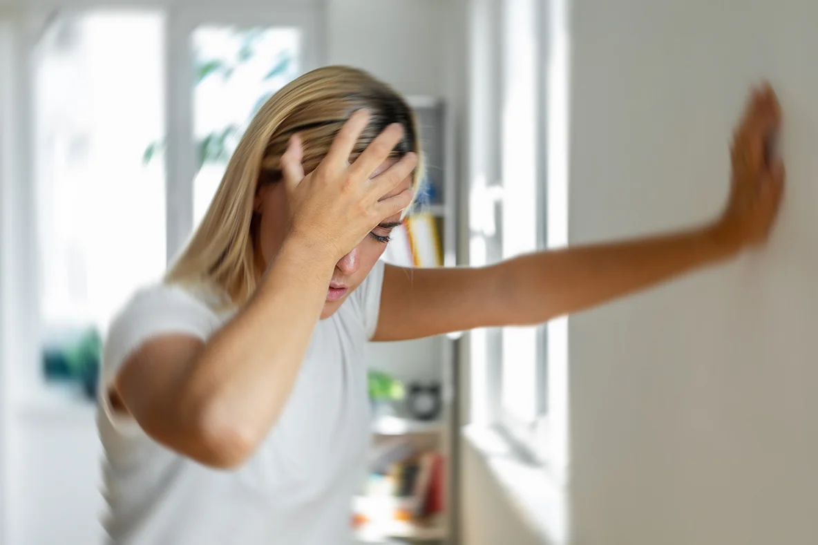 Eine Frau stützt sich an der Wand ab und greift sich mit der anderen Hand an den Kopf.