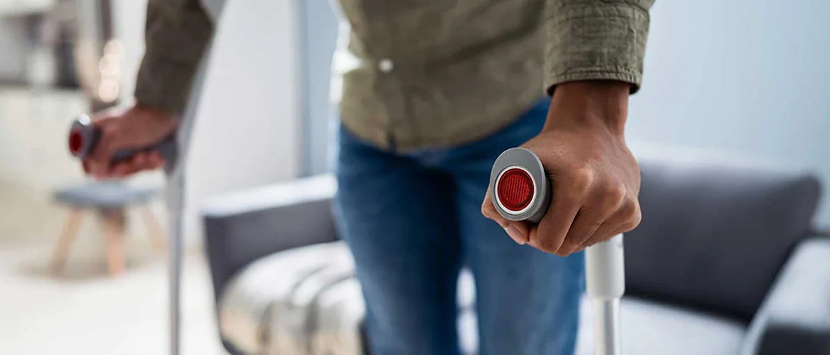 Junge Person mit Krücken steht in Wohnzimmer