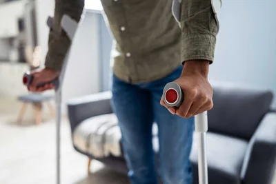 Junge Person mit Krücken steht in Wohnzimmer