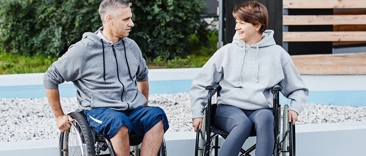 Zwei Personen sitzen im Rollstuhl und unterhalten sich miteinander