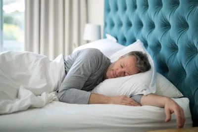 Ein Mann mittleren Alters liegt seitlich schlafend im Bett