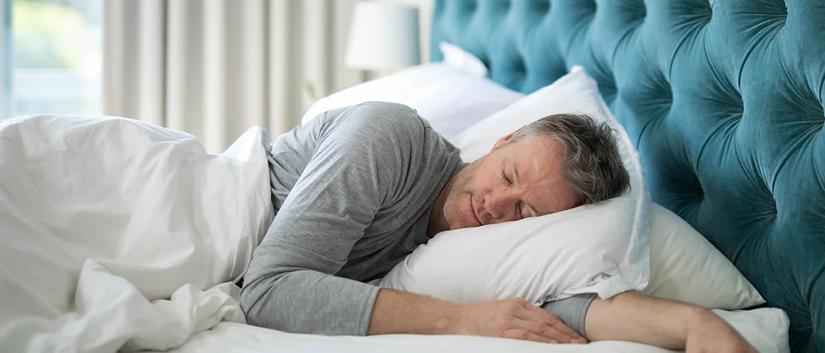 Ein Mann mittleren Alters liegt seitlich schlafend im Bett