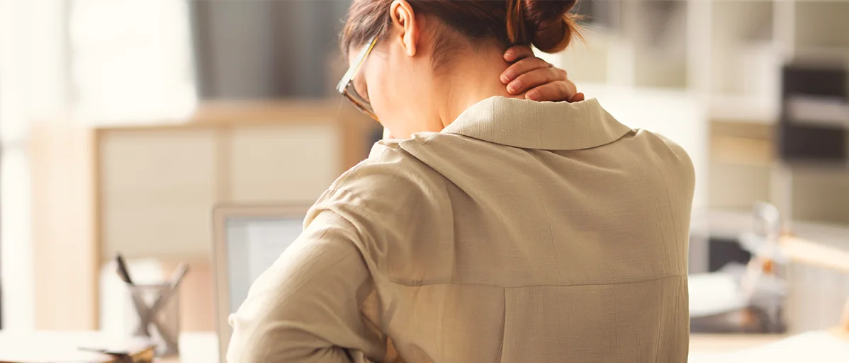 Person die an einem Schreibtisch sitzt und sich in den Nacken greift
