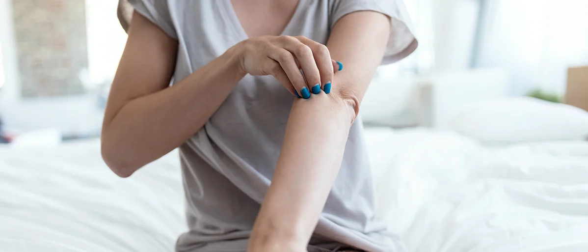 Person sitzt auf einem Bett und greift sich mit der Hand an den Oberarm
