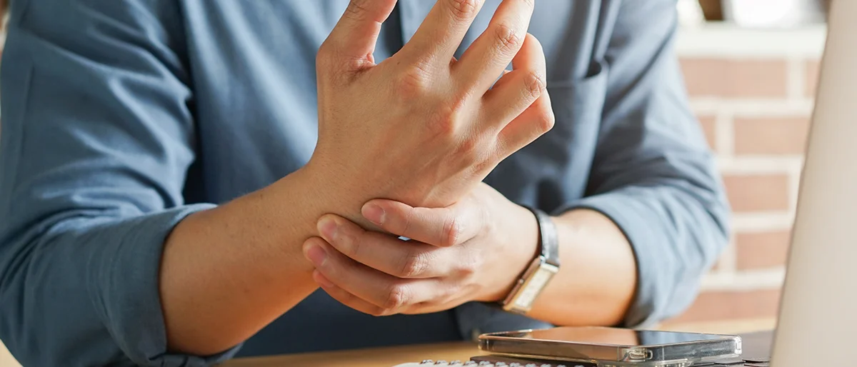 Person vor einem Laptop greift sich an das Handgelenk