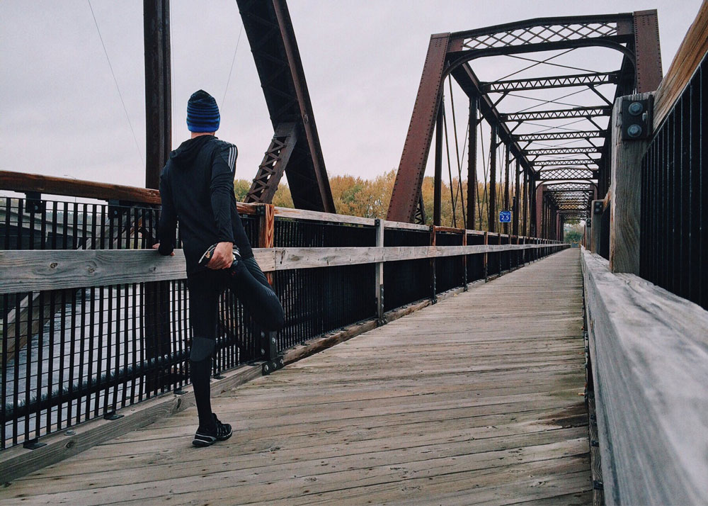 Jogger steht auf einer Brücke und dehnt sich
